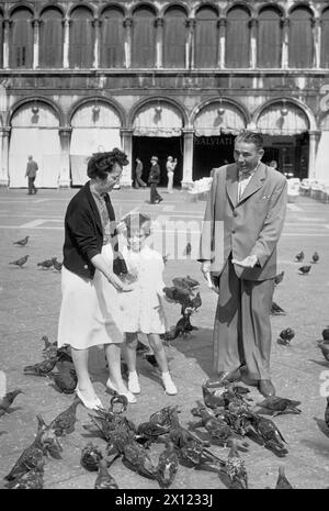 Touristen, Paar und Tochter, Fütterung von Tauben auf dem Markusplatz oder dem Markusplatz, Venedig, Italien. Vintage- oder Historic Schwarzweiß- oder Schwarzweißbild c1960s. Stockfoto