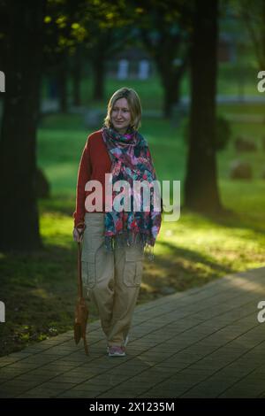 Eine Frau läuft zügig die Parkallee hinunter, ihr Ausdruck bestimmt, während sie sich auf ihren Weg vor dem üppigen Grün konzentriert. Stockfoto