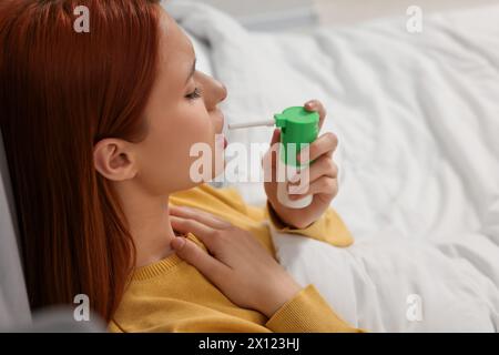 Junge Frau mit Kehlspray im Bett Stockfoto