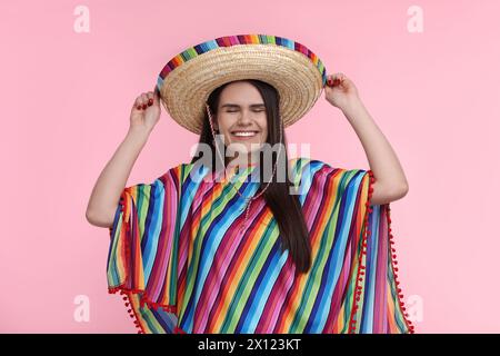 Junge Frau mit mexikanischem Sombrero-Hut und Poncho auf rosa Hintergrund Stockfoto