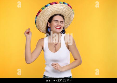 Junge Frau mit mexikanischem Sombrero-Hut, der auf gelbem Hintergrund tanzt Stockfoto