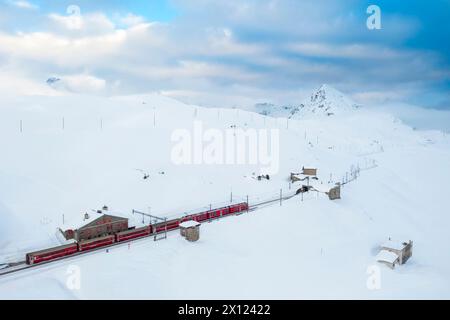 Blick aus der Vogelperspektive auf den berühmten Bernina Express, der im Winter am Bernina Pass vorbeifährt. Graubünden, Engadin, Schweiz. Stockfoto