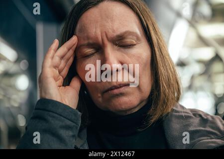Erwachsene kaukasische Frau mit schweren Migräne-Kopfschmerzen, die nachts im Bus mit öffentlichen Verkehrsmitteln fährt, selektiver Fokus Stockfoto
