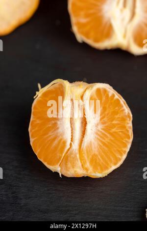 Geschält, Orangen-Mandarinen auf dem Tisch in Nahaufnahme, eine große Anzahl von Orangen-Zitrusfrüchten auf einer schwarzen Schieferoberfläche Stockfoto