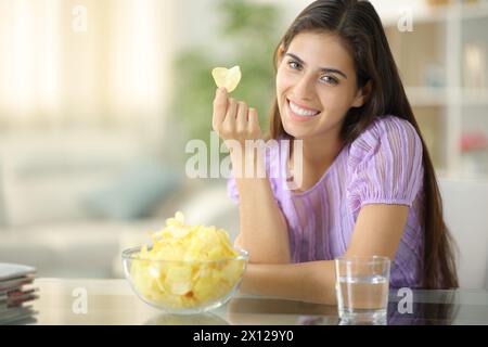 Glückliche Frau sieht dich an, als du Kartoffelchips zu Hause hältst Stockfoto