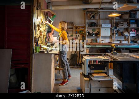 Eine interessierte Handwerkerin, die in der Tischlerei beschäftigt ist, holt Werkzeuge für Holzprodukte. Kleine Unternehmen Stockfoto