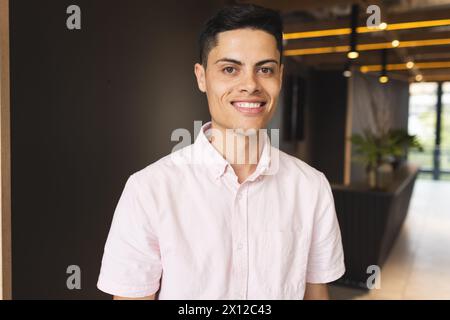 Ein junger, birassischer Mann mit rosa Hemd lächelt in einem modernen Geschäftsbüro Stockfoto