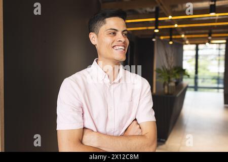 Ein birassischer junger Mann mit rosa Hemd steht, die Arme gekreuzt, lacht Stockfoto