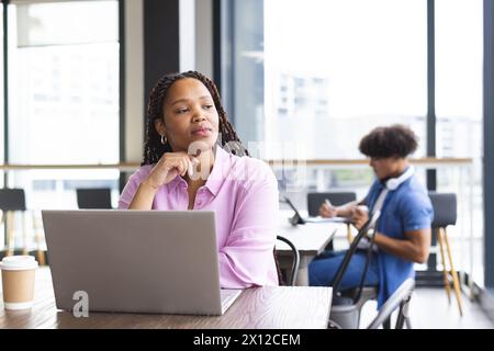 Eine junge Frau mit geflochtenen Haaren arbeitet in einem modernen Geschäftsbüro an einem Laptop Stockfoto