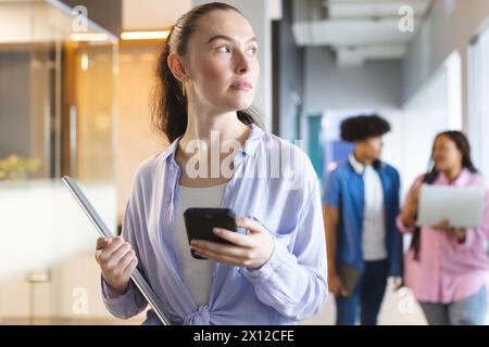 Kaukasische Frau, die ein Smartphone hält, in einem modernen Geschäftsbüro im Flur läuft Stockfoto