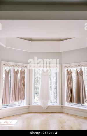 Hochzeitskleid und Brautjungfernkleider hängen im sonnigen Zimmer Stockfoto