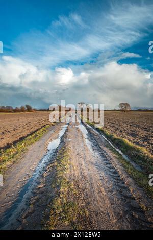 Vertikale Aufnahme einer Feldstraße auf einem gepflügten Feld und Wolken über dem Horizont, Februartag, Ostpolen Stockfoto