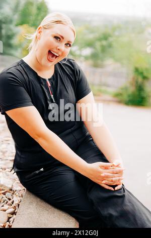 Außenporträt einer jungen Frau in schwarzem Gewächs mit großem Lächeln Stockfoto