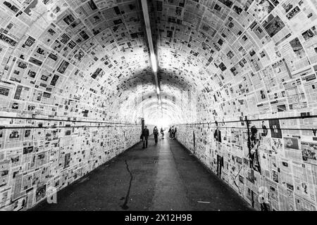 Ein langer Tunnel, der mit alten Zeitungen an den Wänden bedeckt ist, verbindet die Bahnsteige des Bahnhofs in Lugano, Schweiz Stockfoto