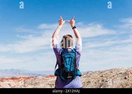 Ein Wanderer in einem lila Hemd macht ein „W“-Zeichen unter dem Wüstenhimmel Stockfoto