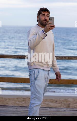 Ein Mann, der zwanglos mit der Mütze nach hinten fährt und Selfie am Strand macht Stockfoto