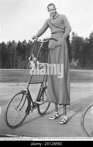 Seltsames Fahrrad mit ebenso seltsamen Radfahrern in den 1940er Jahren Ein Mann, der auf Stelzen gesehen wird, um sein höheres Fahrrad fahren zu können. Seine ebenso lange Hose bedeckt die Stelzen und sie sind in den typischen 1940er Jahren Design Reithose plus Vieren. Die Schuhe und die Knöchel sind schön dekoriert, um den Gesamtlook des seltsamen Mannes zu vervollständigen. 1940 Stockfoto