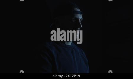 Ernsthafte Männerfigur, die in der dunklen Halle steht und gefährlich aussieht. Schlimme Problemzeit, ein vermummter Kerl fühlt sich verloren und verlassen, wird Geist Stockfoto