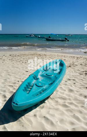 Tropischer Strand in Mexiko mit türkisfarbenen Kajaks auf weißem Sand, blauem Himmel und ruhigem Meer mit Booten im Hintergrund. Idealer Ort für Urlaubssportarten und Stockfoto