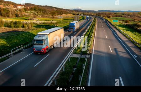 Straßenverkehr. Transportwagen in Schlangen, die auf einer Landstraße unter einem wunderschönen blauen Himmel vorbeifahren Stockfoto