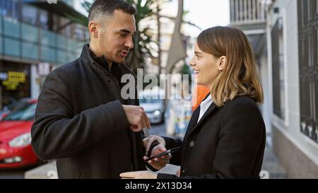 Ein Mann und eine Frau teilen sich einen Moment auf einer Straße der Stadt, während sie gemeinsam auf ein Mobiltelefon vor einem urbanen Hintergrund blicken. Stockfoto