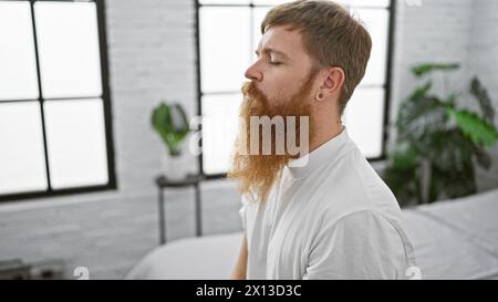 Ruhiger Morgen, junger rothaariger Mann, der sich bequem in einem gemütlichen Bett eingenistet und ruhige Luft einatmet. Ruhig wach, im Schlafzimmer sitzen, ernsthaft konzentriert Stockfoto