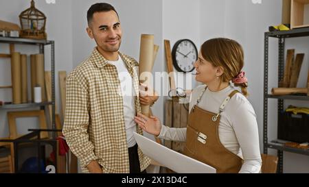 Mann und Frau arbeiten in einer gut organisierten Tischlerei zusammen und bewerten die Holzbaupläne Stockfoto