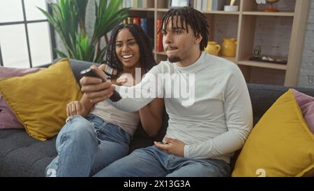 Ein liebevolles Paar genießt die Freizeit, um gemeinsam auf einem gemütlichen Sofa in einem modernen Wohnzimmer des Apartments fernzusehen. Stockfoto