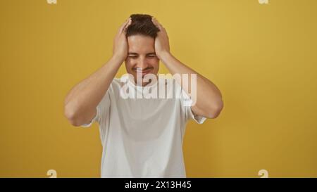 Junger hispanischer Mann in einem weißen T-Shirt, der Frustration vor einem glatten gelben Hintergrund zeigt. Stockfoto