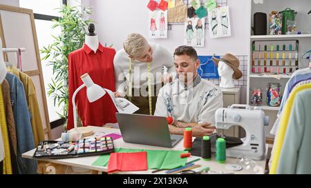 Zwei Schneider, ein Mann und eine Frau, arbeiten in einem lebhaften Schneidergeschäft mit bunten Stoffen und einer Schaufensterpuppe zusammen. Stockfoto