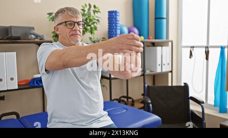 Ein grauhaariger Mann übt seine Arme in einer Physiotherapie-Klinik aus, was auf Gesundheitsfürsorge, Rehabilitation und Seniortätigkeit hinweist. Stockfoto