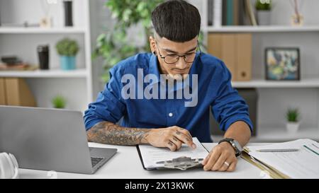 Hübscher junger lateinarbeiter, der in das Lesen von Dokumenten vertieft ist und einen Geschäftsvertrag an seinem beruflichen Arbeitsplatz unterzeichnet Stockfoto