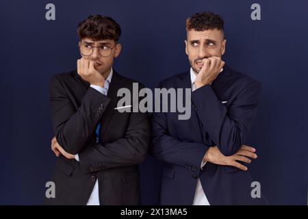 Zwei hispanische Geschäftsmänner in Geschäftskleidung, die gestresst und nervös aussehen, mit Händen auf den Mund beißen Nägeln. Angstproblem. Stockfoto