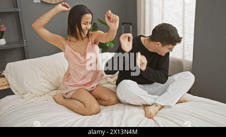 Ein glückliches Paar im Pyjama, das zusammen auf einem Bett in einem gemütlichen Schlafzimmer tanzt und Liebe und Verbundenheit in Innenräumen zum Ausdruck bringt Stockfoto