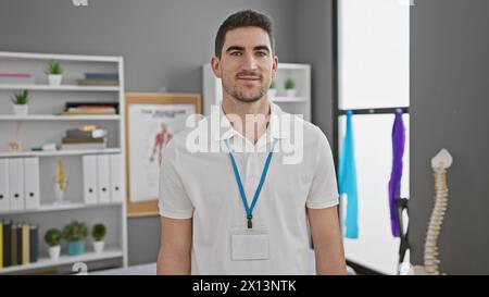 Porträt eines lächelnden jungen Mannes, der ein Schlüsselband trägt und selbstbewusst in einer hellen modernen Klinik steht. Stockfoto