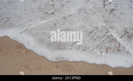 Schäumende Wellen, die sanft über den Sandstrand gleiten und an Gelassenheit und Natur erinnern. Stockfoto