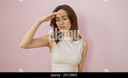 Eine junge hispanische Frau zeigt einen subtilen Ausdruck, posiert vor einem rosafarbenen Hintergrund, der Eleganz und Ruhe weckt. Stockfoto