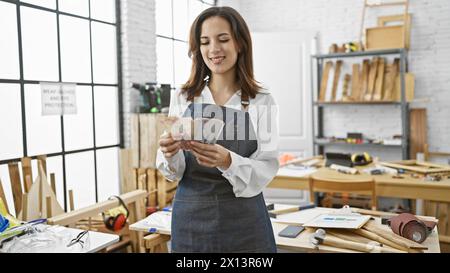 Eine junge Frau zählt kolumbianische Pesos in einer gut beleuchteten Tischlerei. Stockfoto