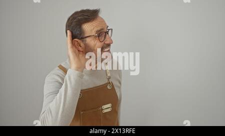 Ein reifer Mann mit Brille und Bart in einer Schürze lächelt und hört auf weißem Hintergrund. Stockfoto