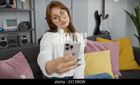 Eine junge kaukasische Frau nimmt zu Hause ein Selfie mit einer gemütlichen Einrichtung mit farbenfrohen Kissen und modernem Dekor auf. Stockfoto