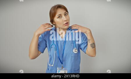 Eine nachdenkliche junge Frau in blauen medizinischen Peelings mit einem Stethoskop vor weißem Hintergrund Stockfoto