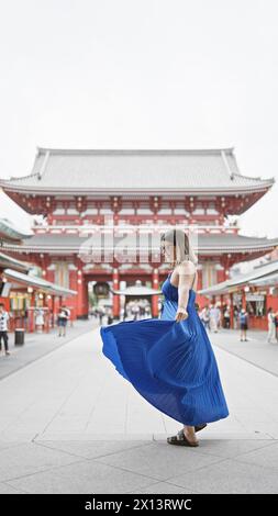 Die sprudelnde hispanische Frau tanzt fröhlich und dreht sich in wunderschönem Kleid inmitten der herrlichen Architektur des Senso-JI-Tempels in tokio. Sie ist durch japan gereist Stockfoto