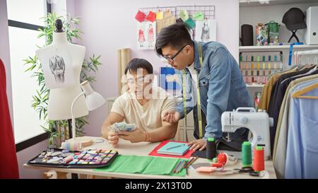 Zwei Männer zählen chinesischen Yuan in einer Schneiderei, umgeben von Designskizzen und einer Nähmaschine Stockfoto