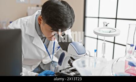 Asiatischer Mann im Labor, der Proben mit Mikroskop im wissenschaftlichen Forschungsumfeld analysiert. Stockfoto