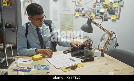 Ein konzentrierter junger Mann arbeitet in einem geschäftigen Detektivbüro, umgeben von Beweismitteln, Hinweisen und Ermittlungsdokumenten. Stockfoto