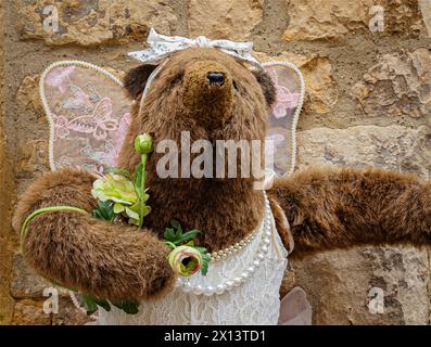 Ein großer, kuscheliger brauner Bär, der ein Kleid mit Engelsflügeln und einem Perlenhalsausschnitt trägt. Dating, Ehe, ausgehen, Geschlecht oder Identitätskonzept Stockfoto