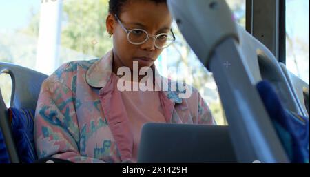 Abstrakte bunte Formen gegen afroamerikanerin, die im Bus einen Laptop benutzt Stockfoto