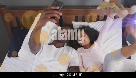Bild von Lichtflecken über dem afroamerikanischen Mann und seiner Tochter, die Selfies machen Stockfoto