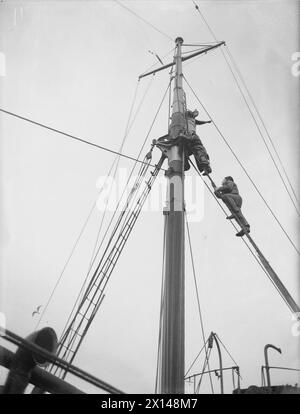 MIT EINEM TRAWLER AUF DER NORDPATROUILLE. MAI 1942 AN BORD DES HM TRAWLERS NORTHERN SKY, DER VON SCAPA AUS AUF DER NORDPATROUILLE OPERIERT. MITGLIEDER DER BESATZUNG DER HMS NORTHERN SKY BEI EINEM DER HÄRTESTEN AUFGABEN AUF SEE, DER NORTHERN PATROUILLE. - Der Blick im Krähennest, ein kleines Objekt, das ein paar hundert Meter entfernt schwimmt. Unter ihm sind zwei Seeleute, die die Takelage umbauen Stockfoto