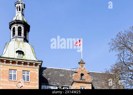 Dänische Flagge auf dem Dach eines Gebäudes vor blauem Himmel. Stockfoto